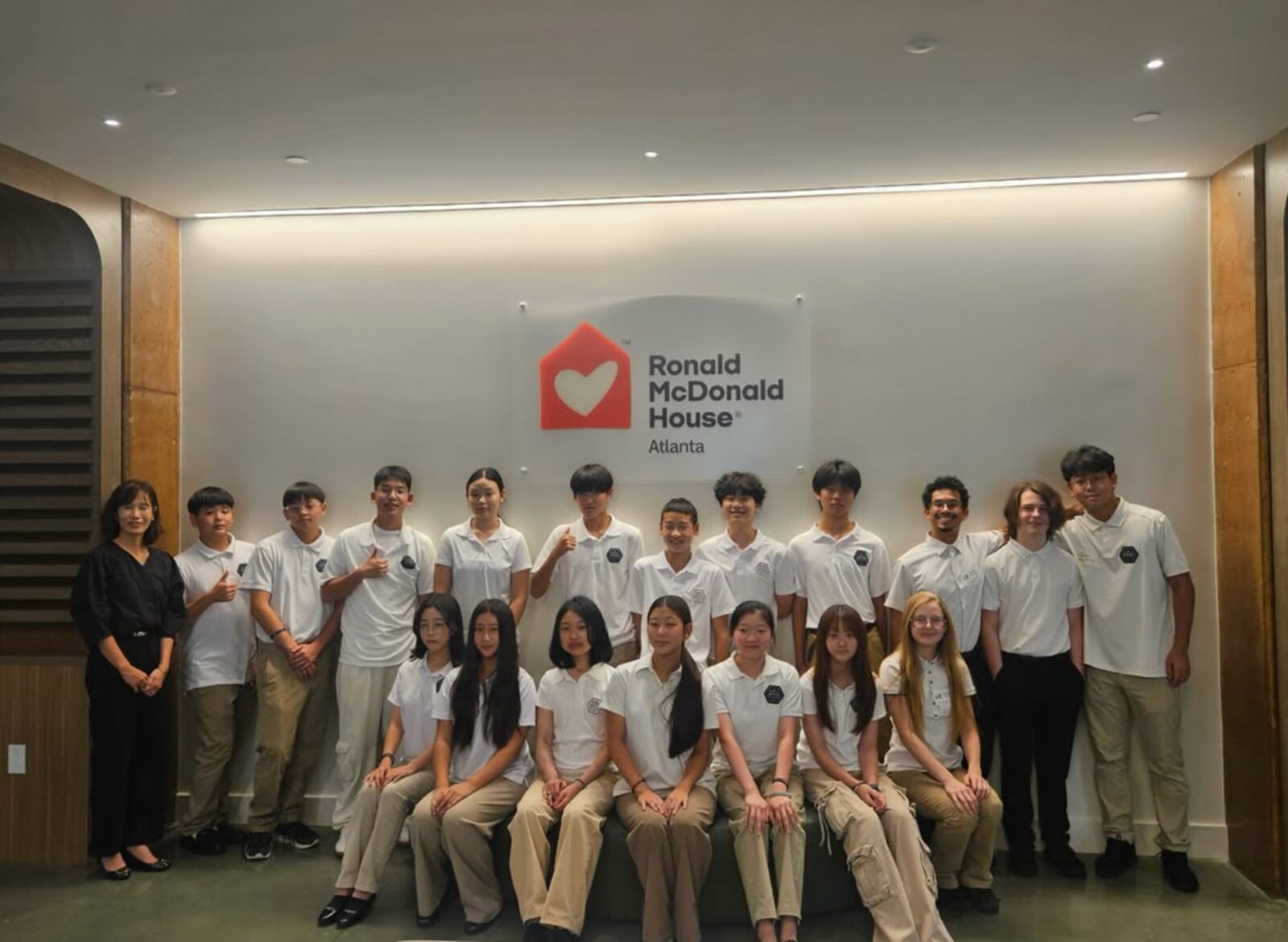 GYCO students in white polos with their advisor, gathered under the Ronald McDonald House Atlanta sign after a visit