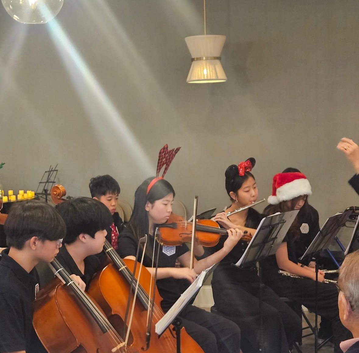 Students in festive holiday hats performing a Christmas concert with cellos, viola, and flute for a senior community