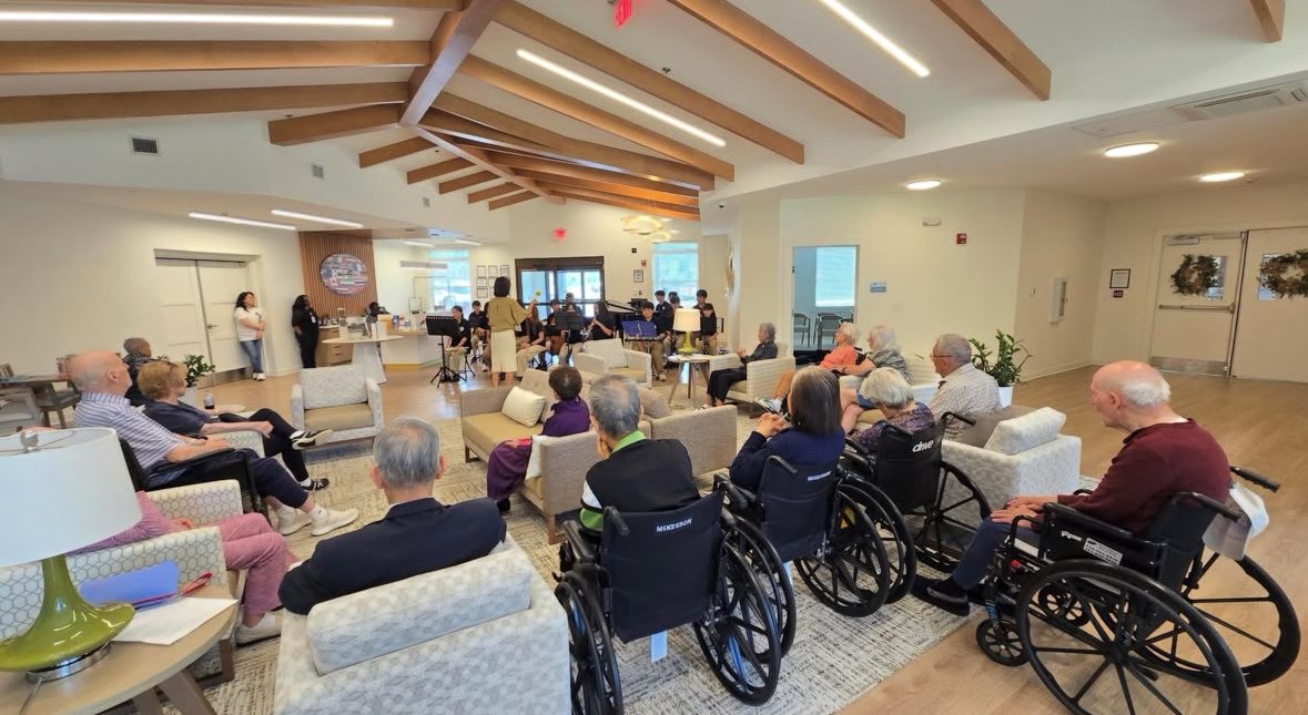 Residents of a senior community, some in wheelchairs, gathered to hear the student ensemble perform in their community room