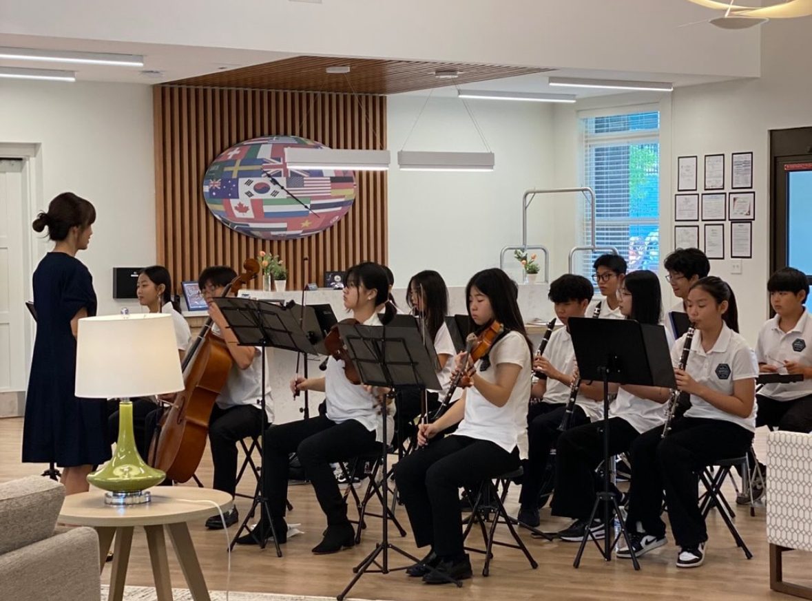 Student ensemble performing with strings and clarinets before an international flag display at a partner community