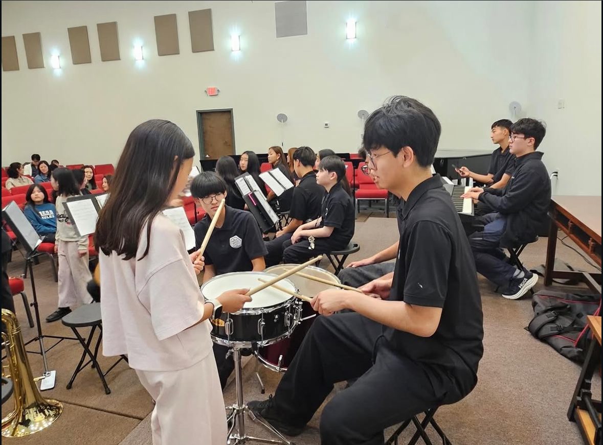 An older student teaching a younger student snare drum rhythms during an ensemble rehearsal