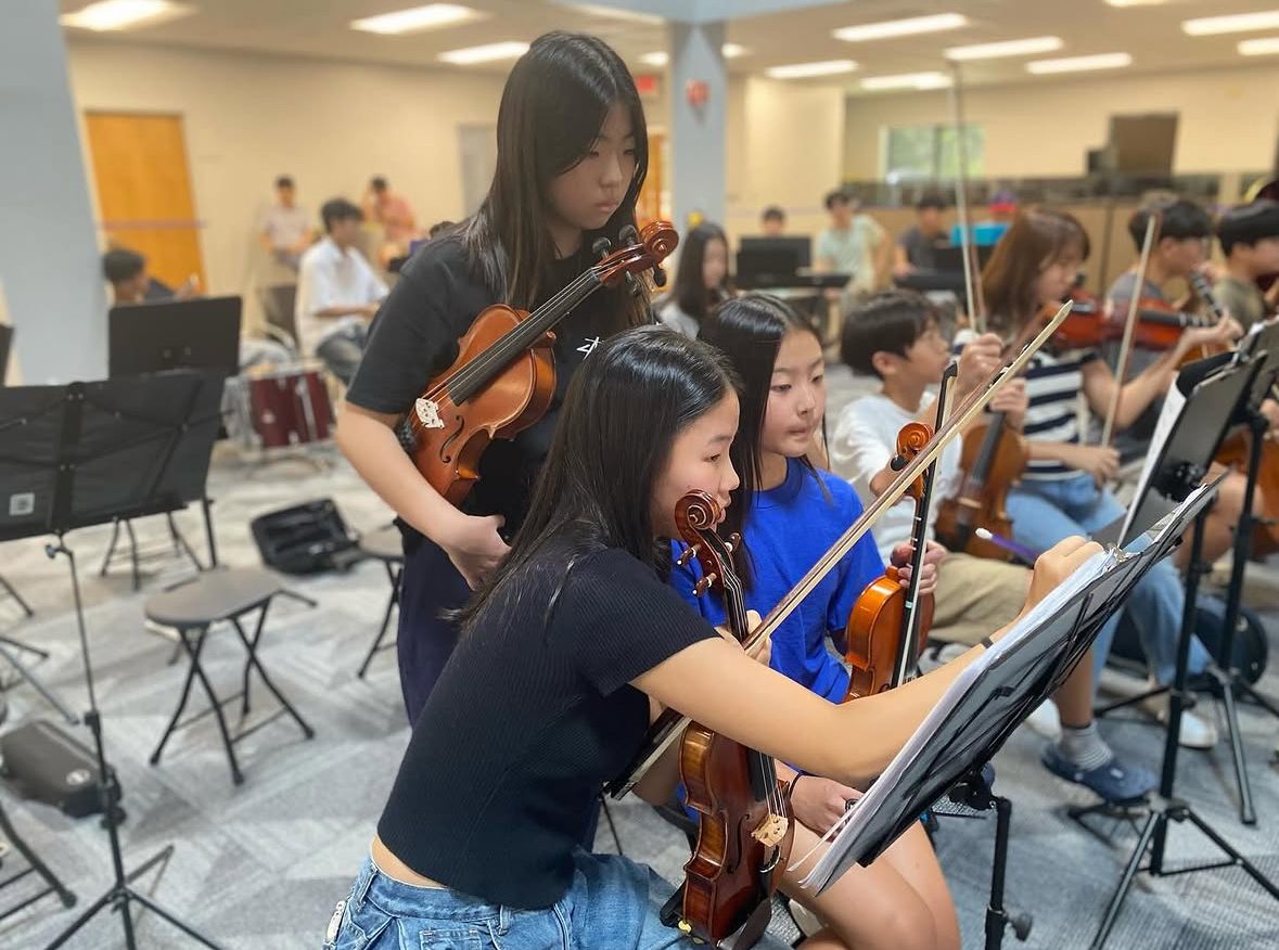 Student violinists coaching younger players through their part at a rehearsal