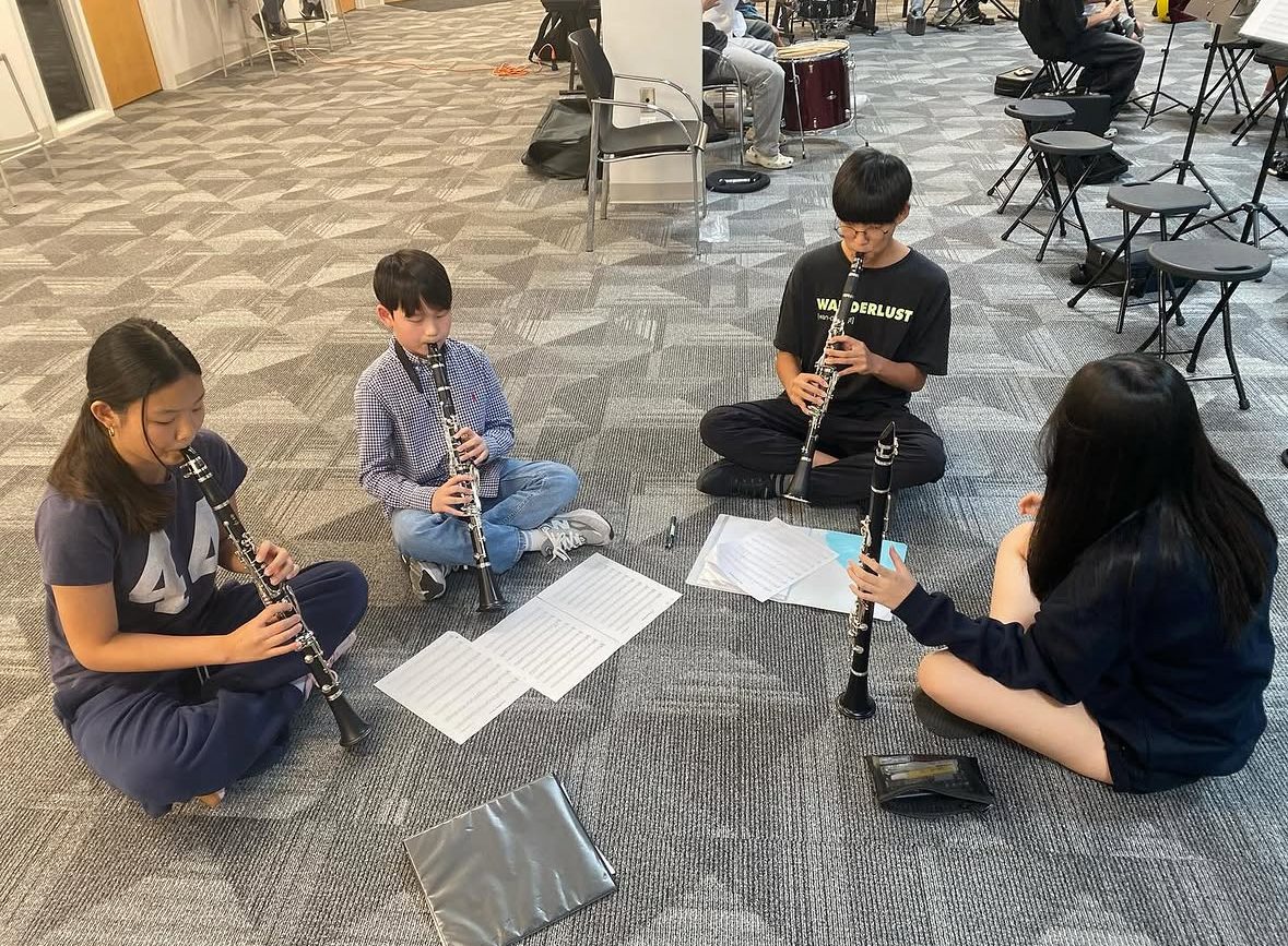 Four clarinet students practicing together in a circle with sheet music between them