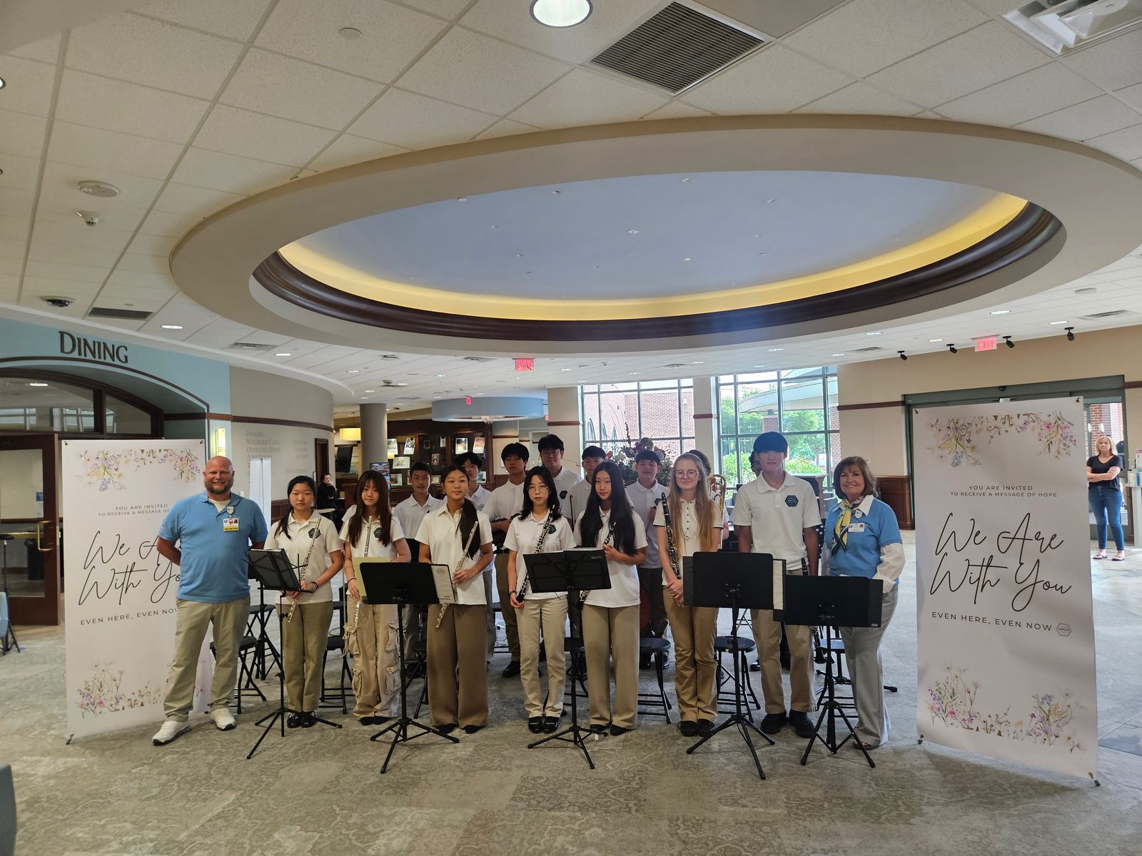Student musicians standing with hospital volunteers between two We Are With You banners after a performance at City of Hope Atlanta