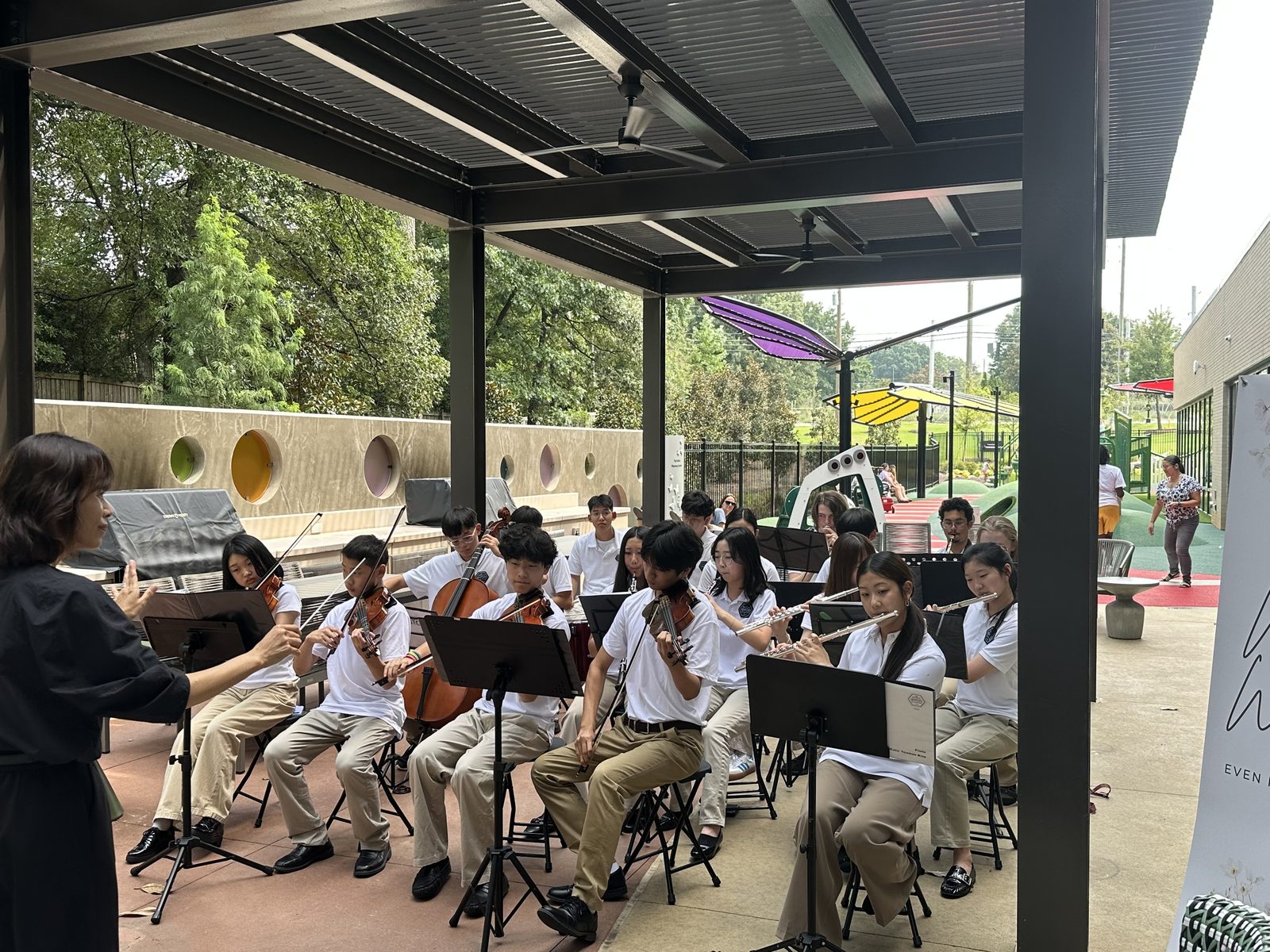 Student orchestra performing under the pergola at Ronald McDonald House Atlanta with the playground behind them