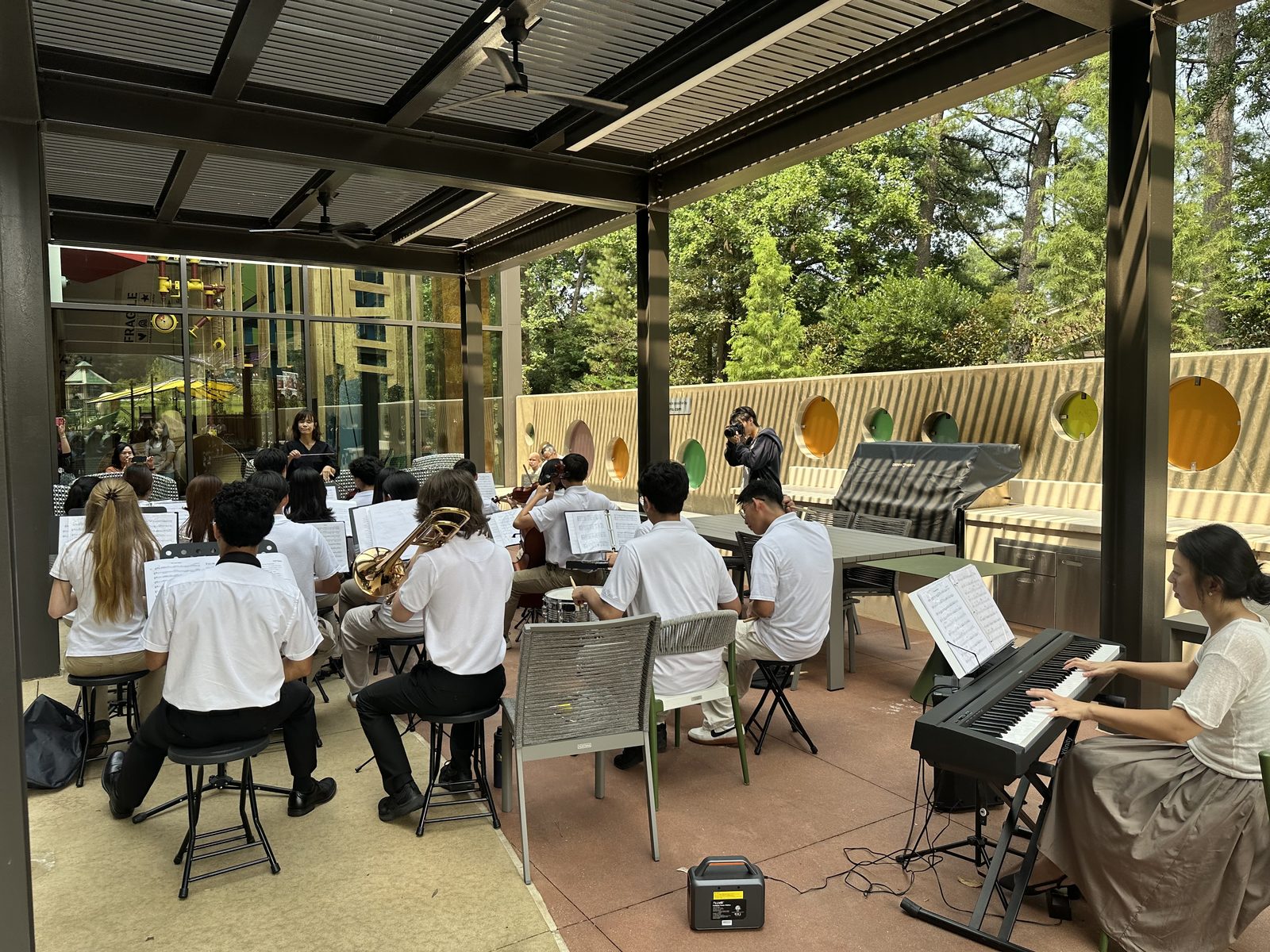 Full ensemble with keyboard, trombone, strings, and percussion performing in the outdoor kitchen at Ronald McDonald House Atlanta